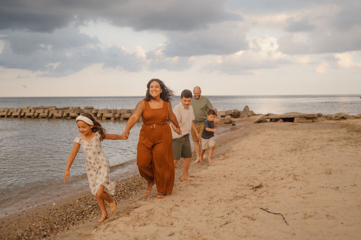 A group of people in warm sunset light walk joyfully along a beach shoreline with stone barriers in the water.