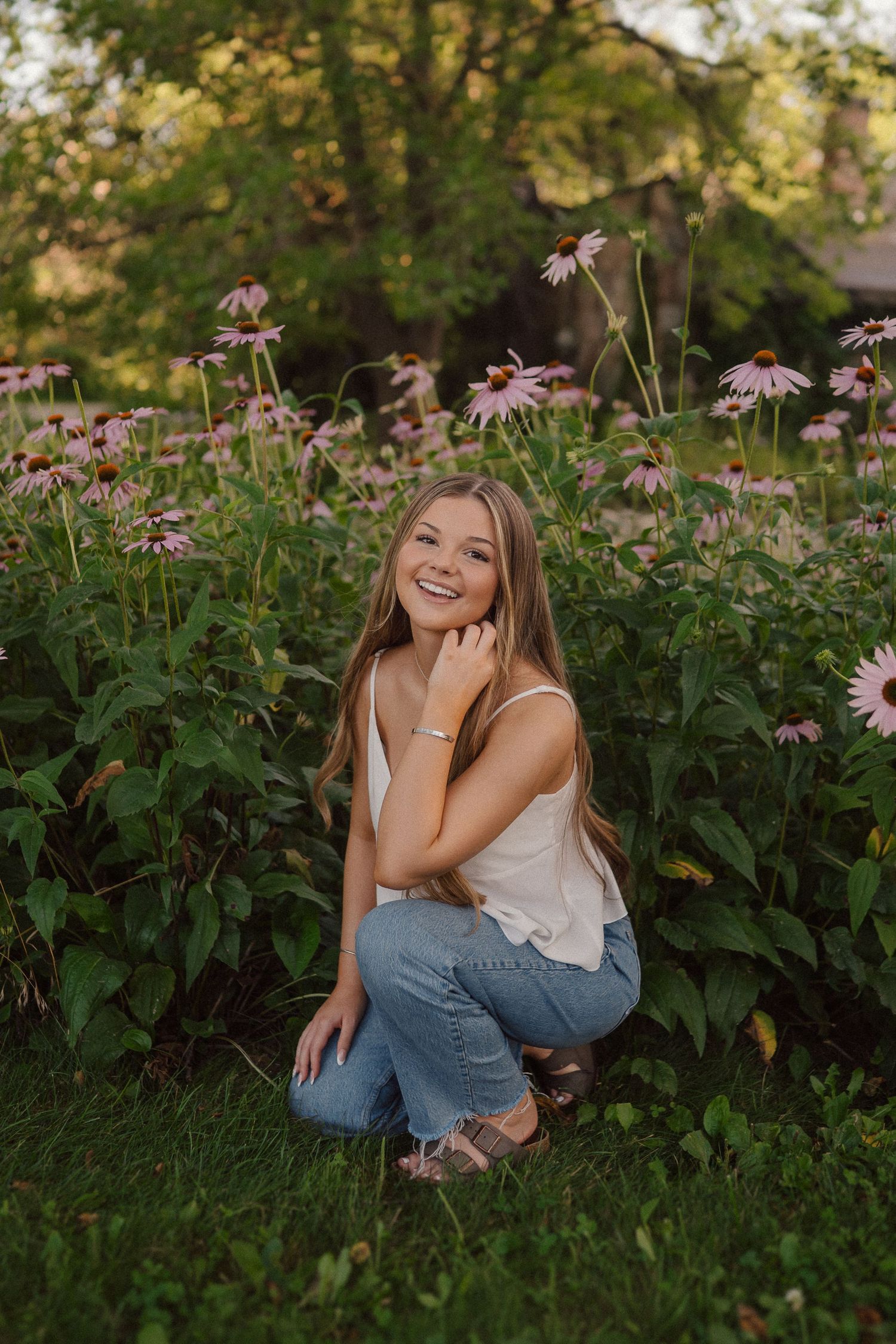 A casual outdoor portrait with pink coneflowers and greenery in a natural garden setting during golden hour.