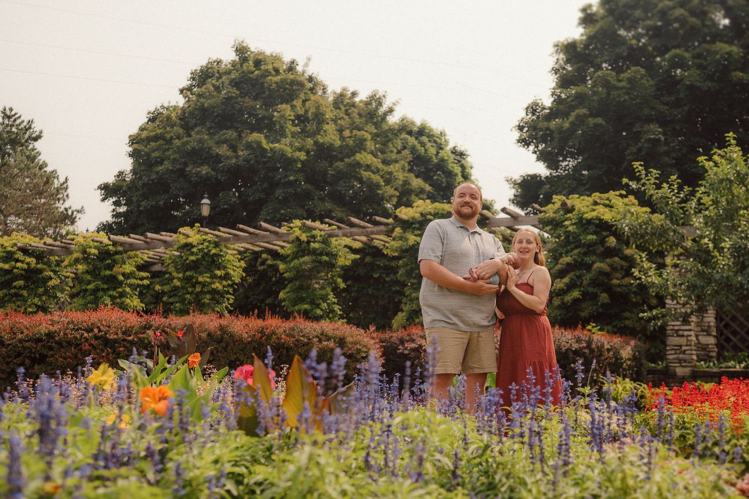 A couple shares a romantic moment in a vibrant flower garden blooming with purple and orange blossoms at sunset.