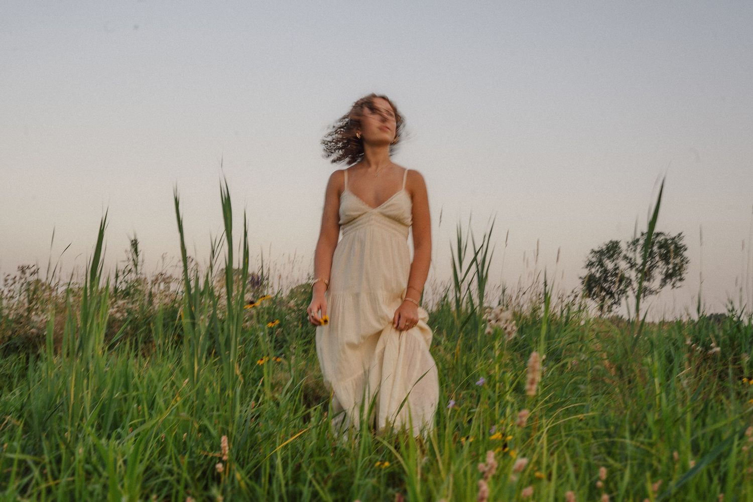 Woman in a dress dancing in a rustic field at dusk.