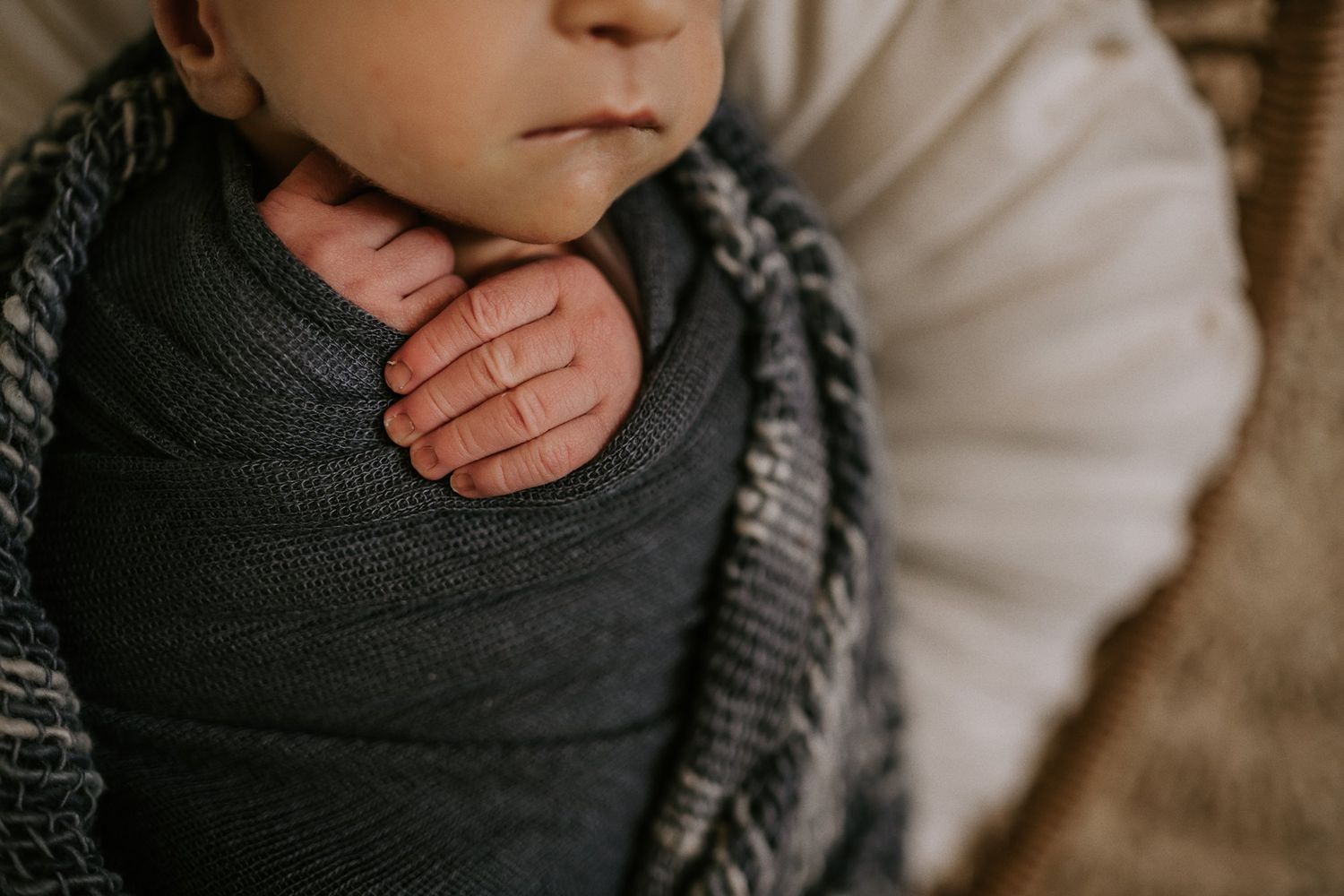 Close-up detail of a swaddled newborn with a gentle hand resting on their chest.