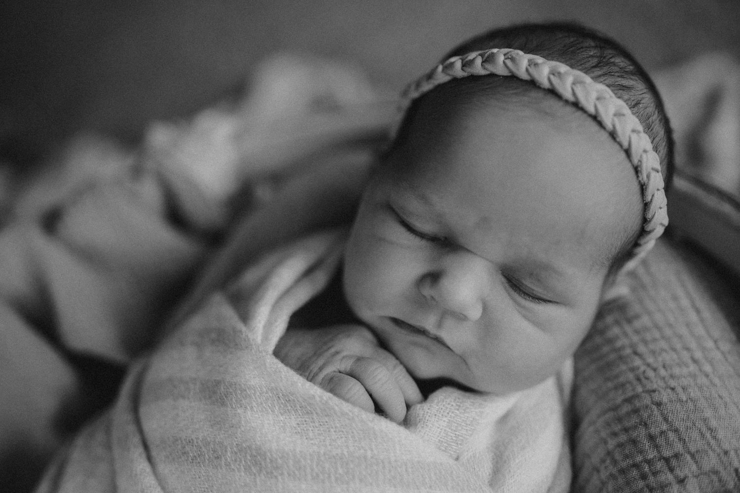 Black and white portrait of sleeping infant with braided headband wrapped in soft fabric.