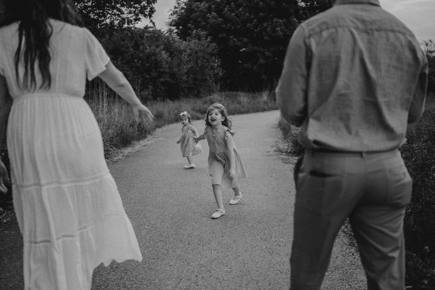 A candid black and white photo captures a running child between adults on a country path.