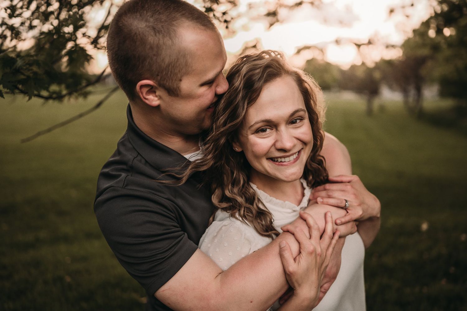 Romantic couple embraces in a sunlit park during golden hour photography session.