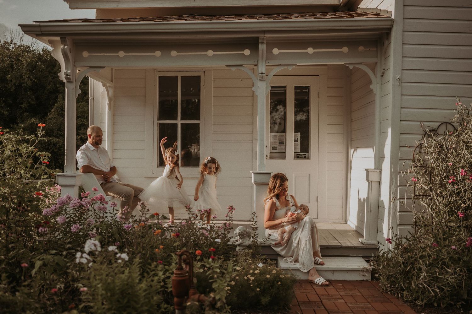 A rustic farmhouse porch serves as backdrop for an elegant family portrait in white dresses.