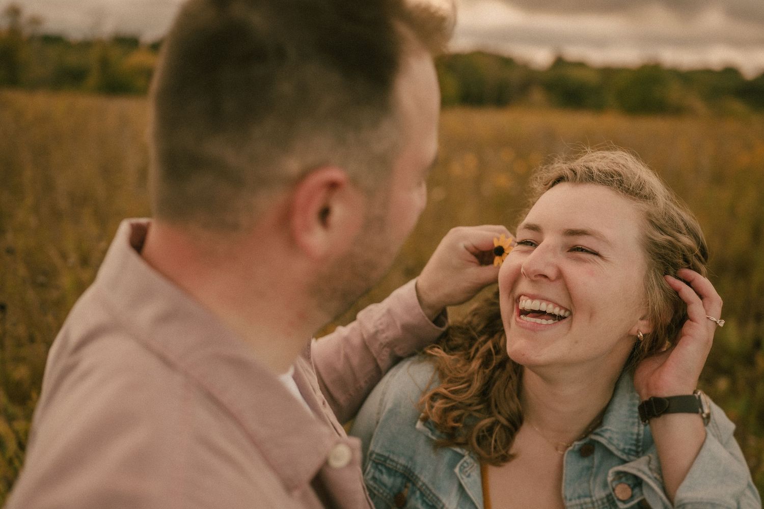 A romantic moment captured between a couple laughing together in a golden field at sunset.