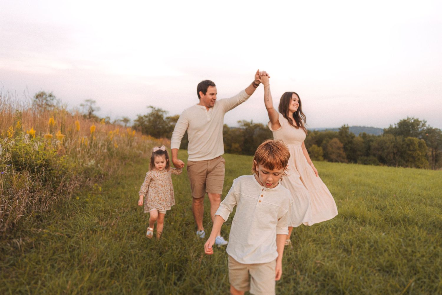 Family holding hands while walking through a scenic meadow at sunset.