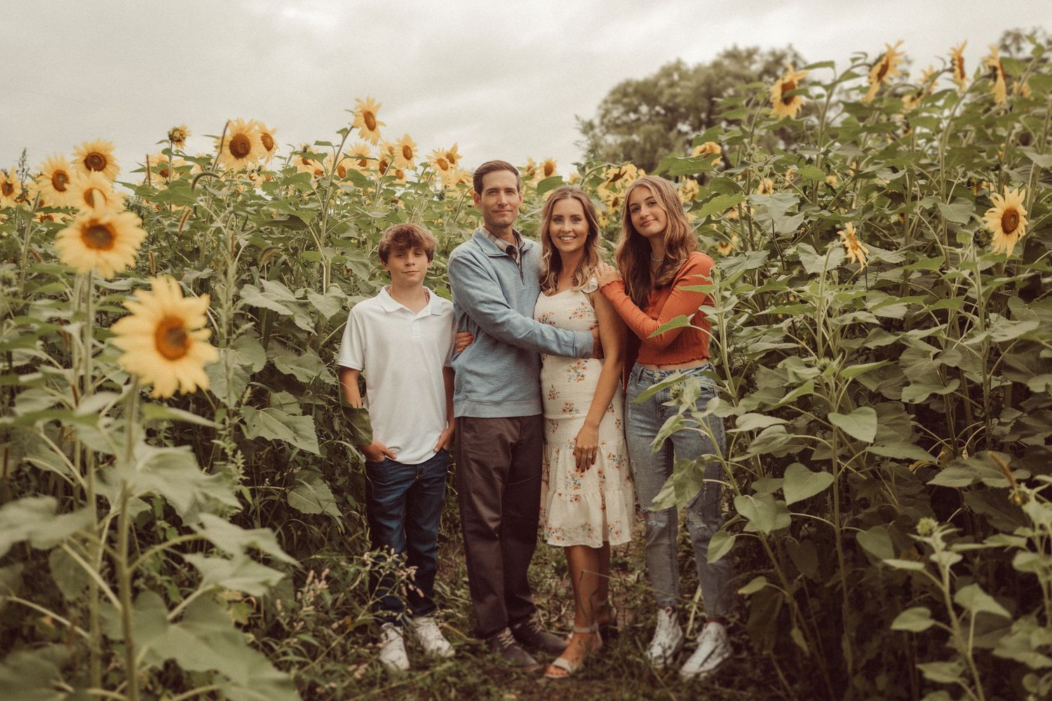 A family poses together in front of tall sunflowers on an overcast day.