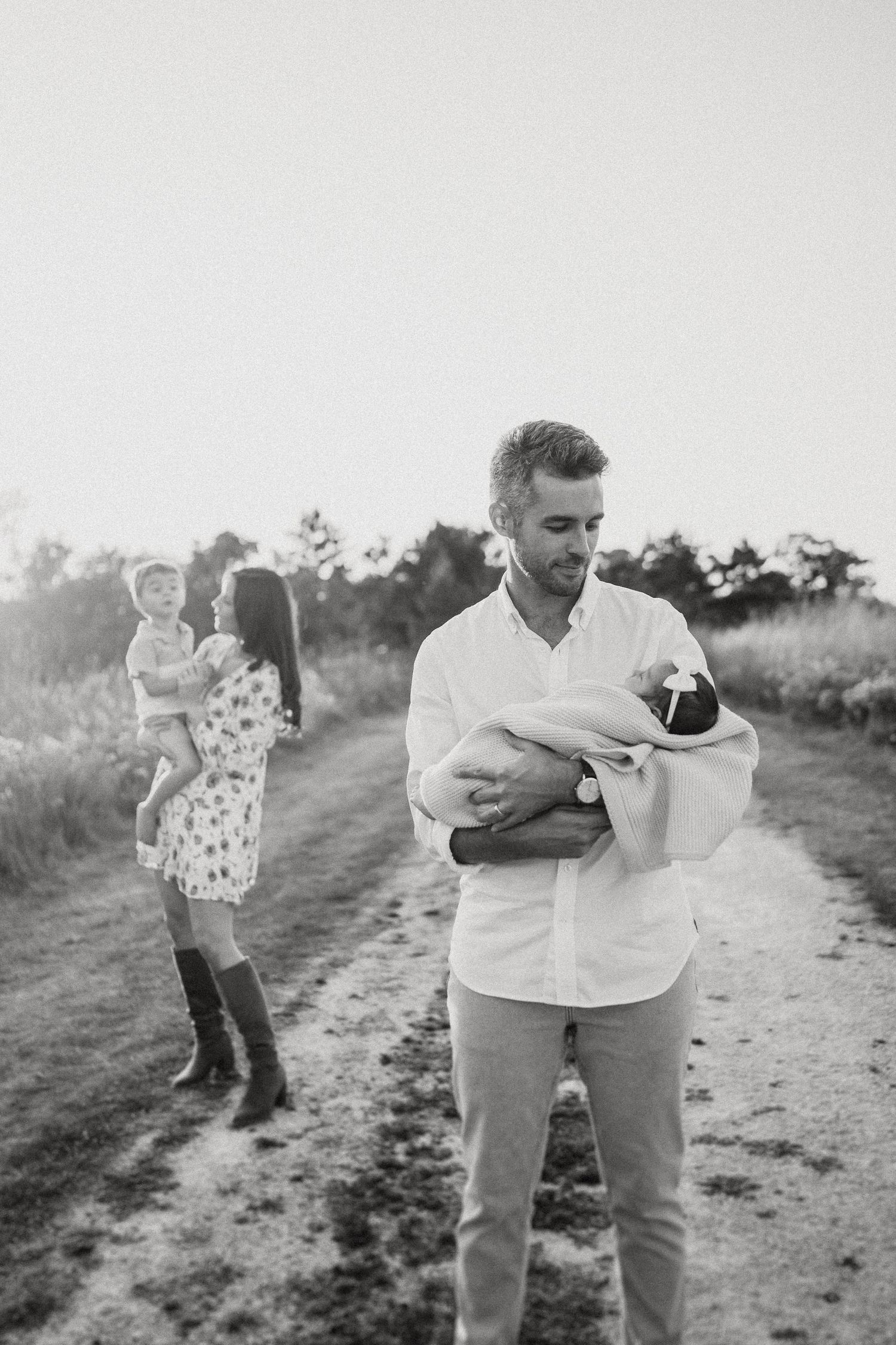 A tender family moment captured on a dirt path during golden hour in a natural outdoor setting.