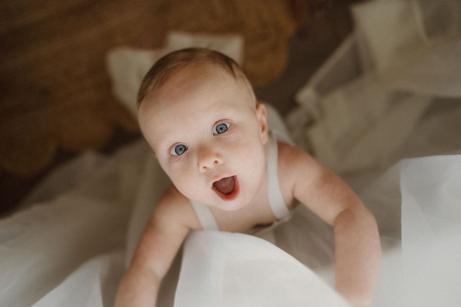 Close-up of baby surrounded by white fabric during indoor photoshoot.
