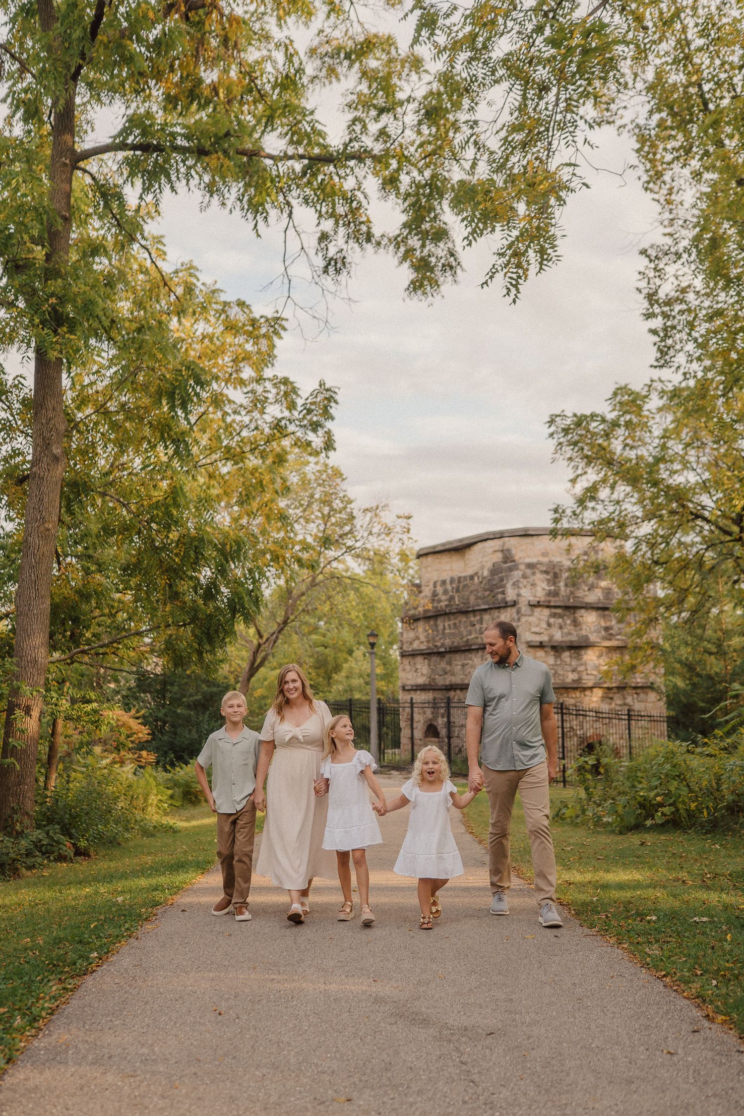 Family walking together on an autumn path with stone buildings and fall foliage in the background.