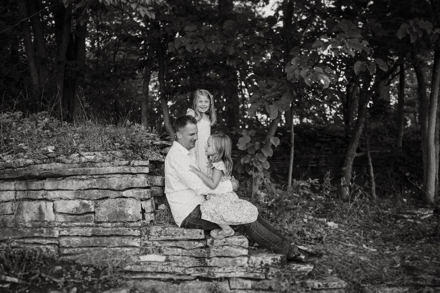 Black and white portrait on stone steps surrounded by lush forest scenery.