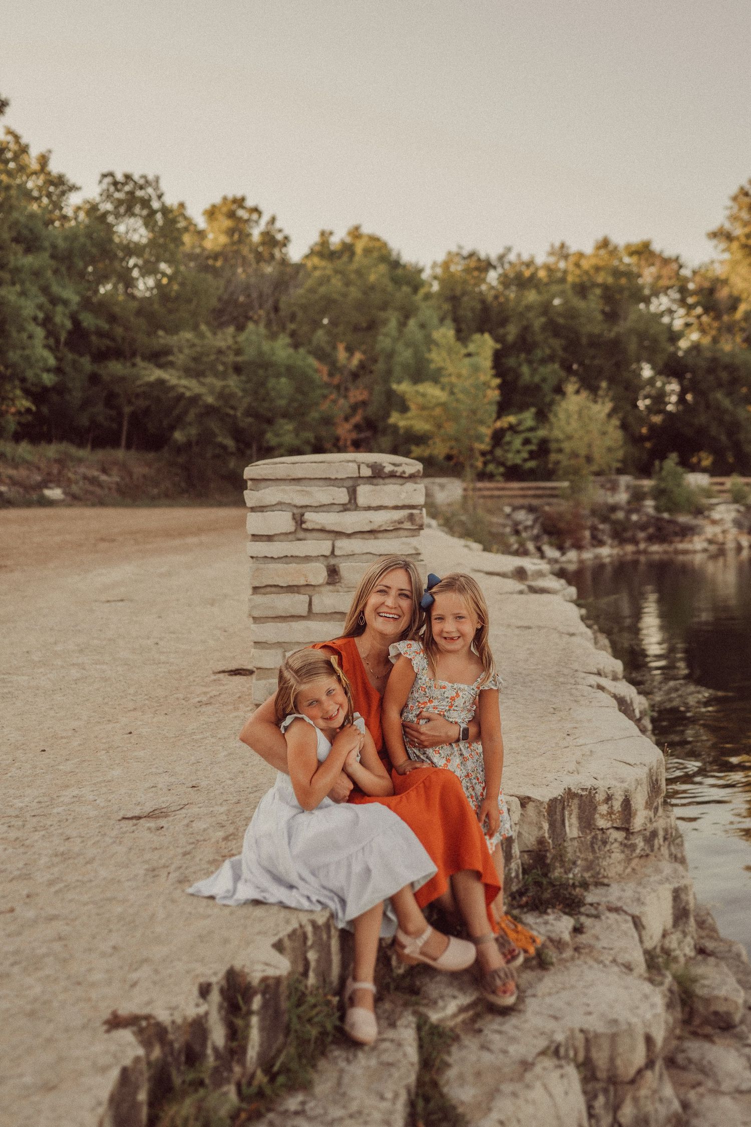Golden hour portrait session by a lake with stone pillars and warm autumn colors in the background.