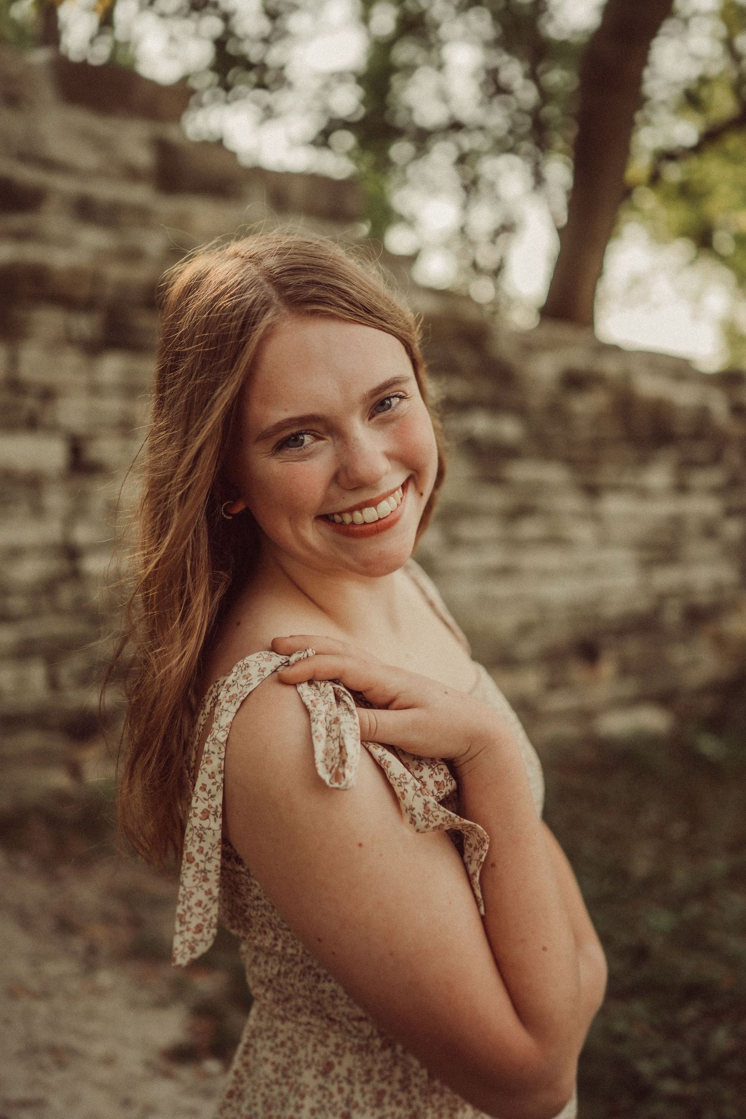 Natural portrait of a woman in a textured dress smiling against stone wall background.
