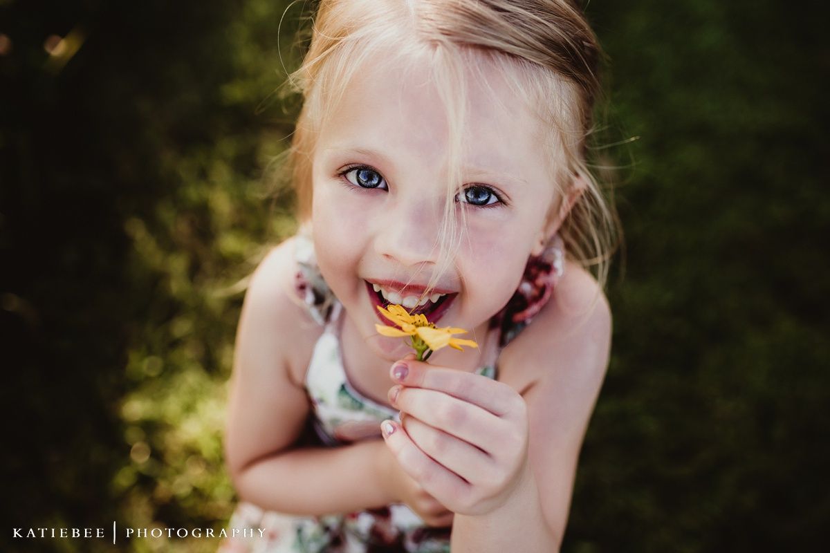 Candid outdoor portrait with bright smile and yellow flower.