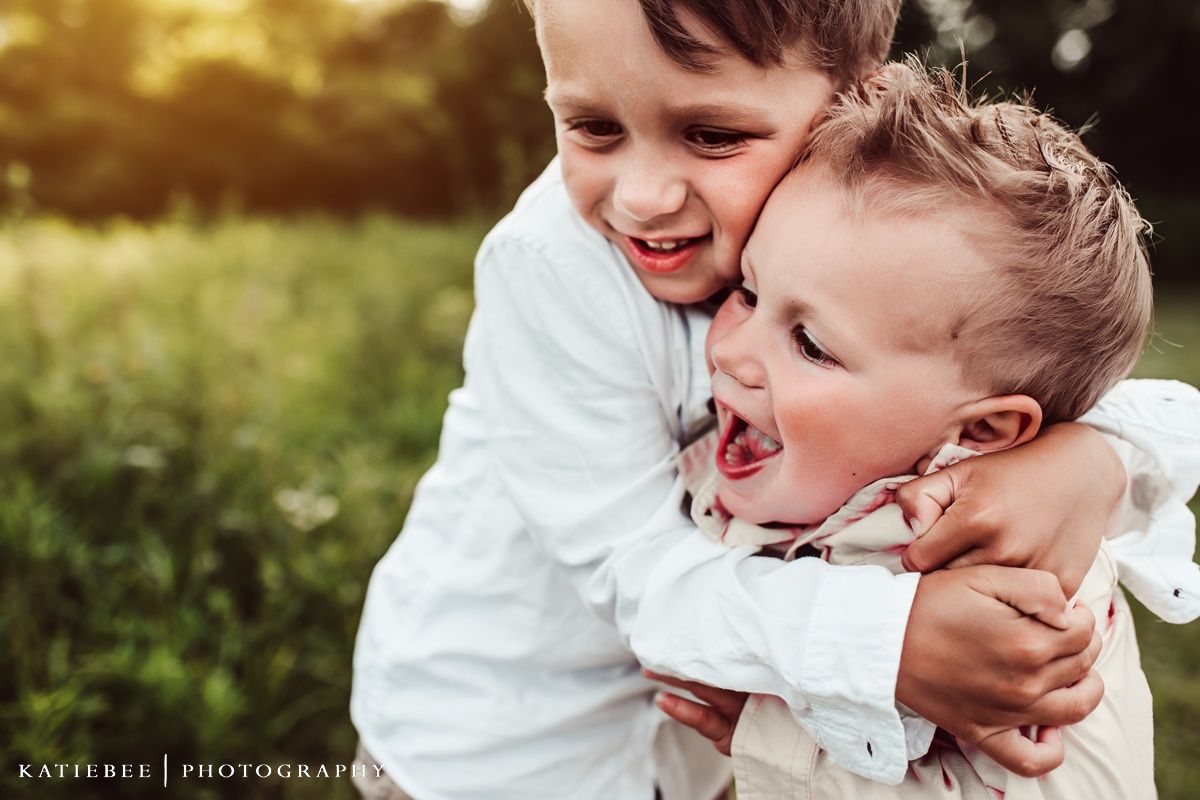 Two children sharing genuine laughter and embrace in golden sunlit setting.