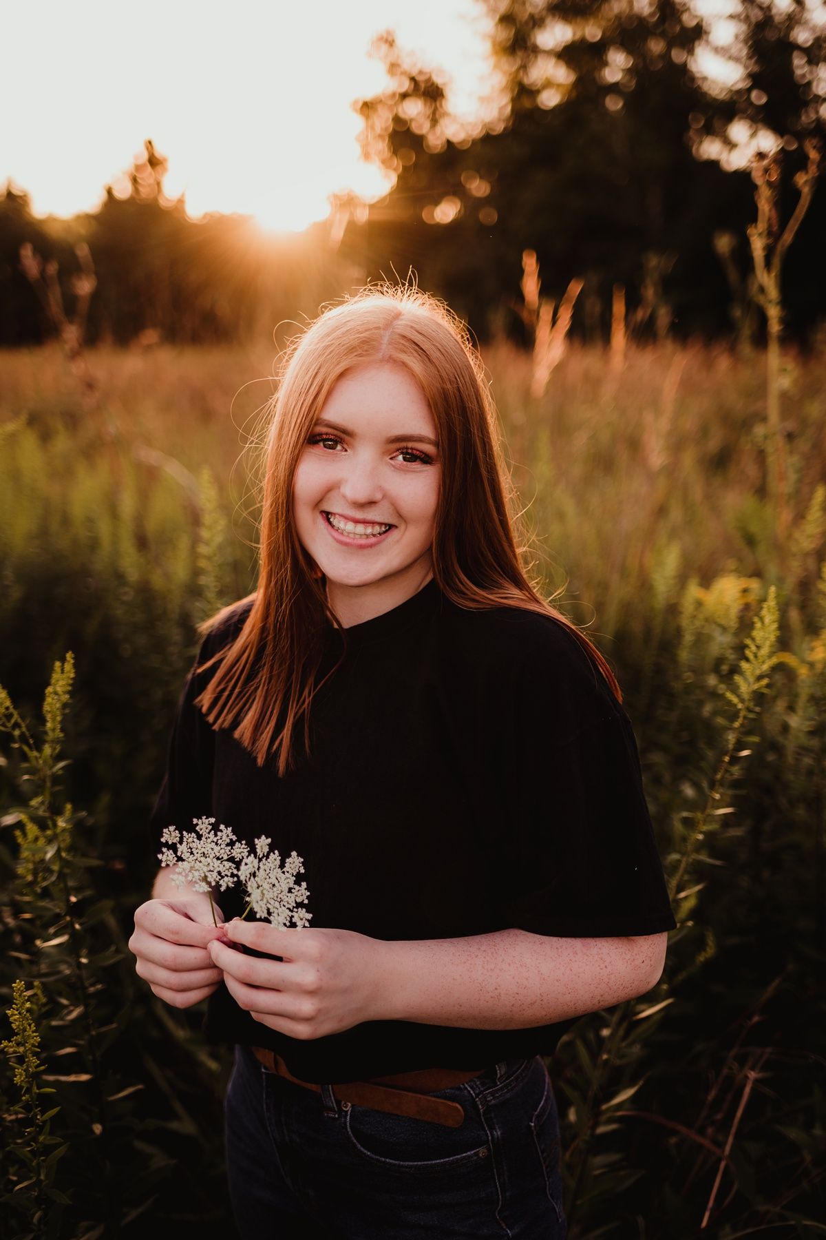 Natural portrait in black shirt holding wildflowers during golden hour.
