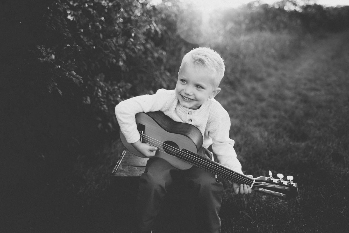 Black and white photo of youth playing guitar while sitting outdoors.