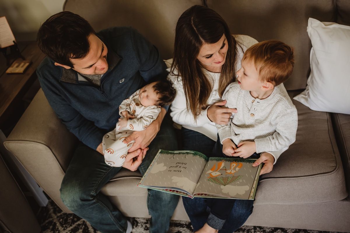 Family reading storybook together while cuddling on grey couch.