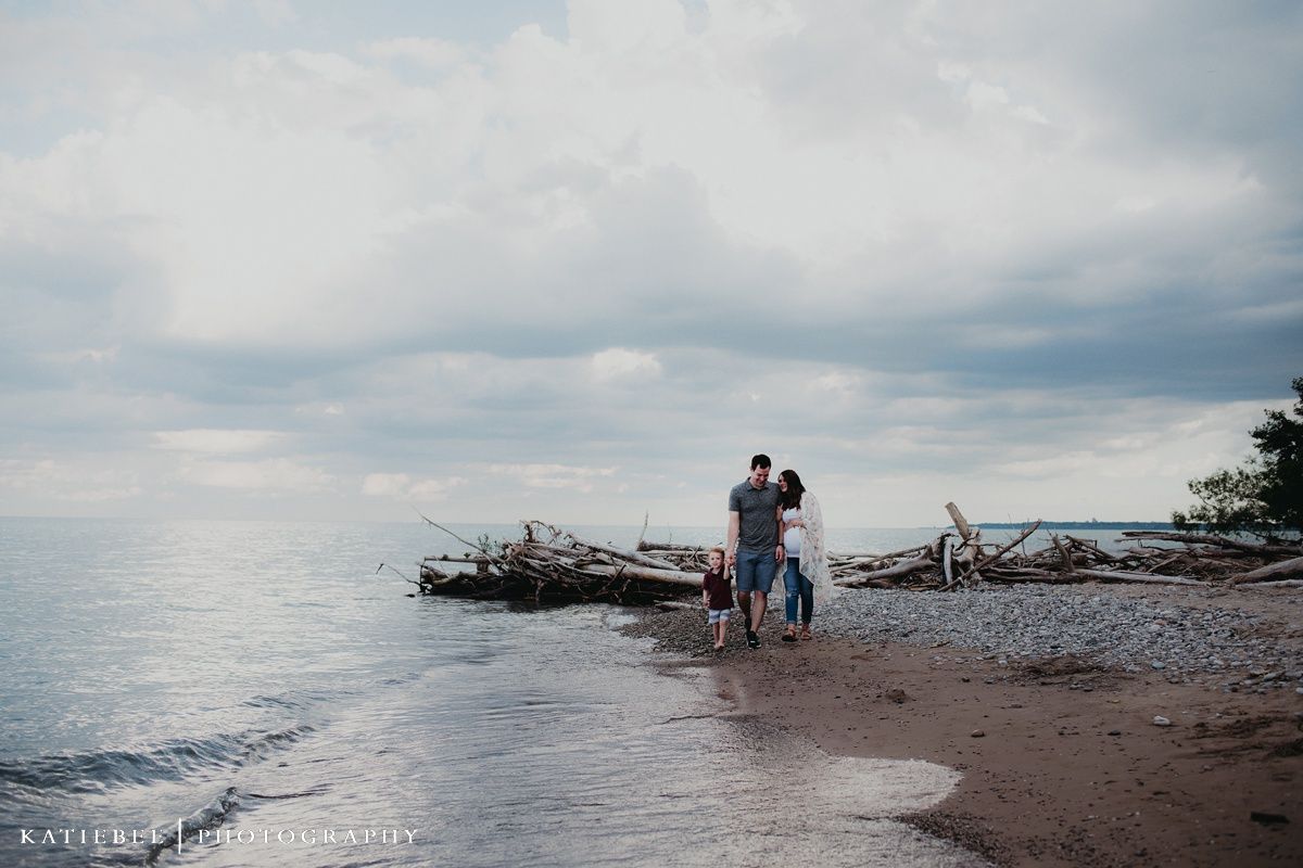 A silhouetted couple stands on a beach with driftwood and cloudy skies at dusk.