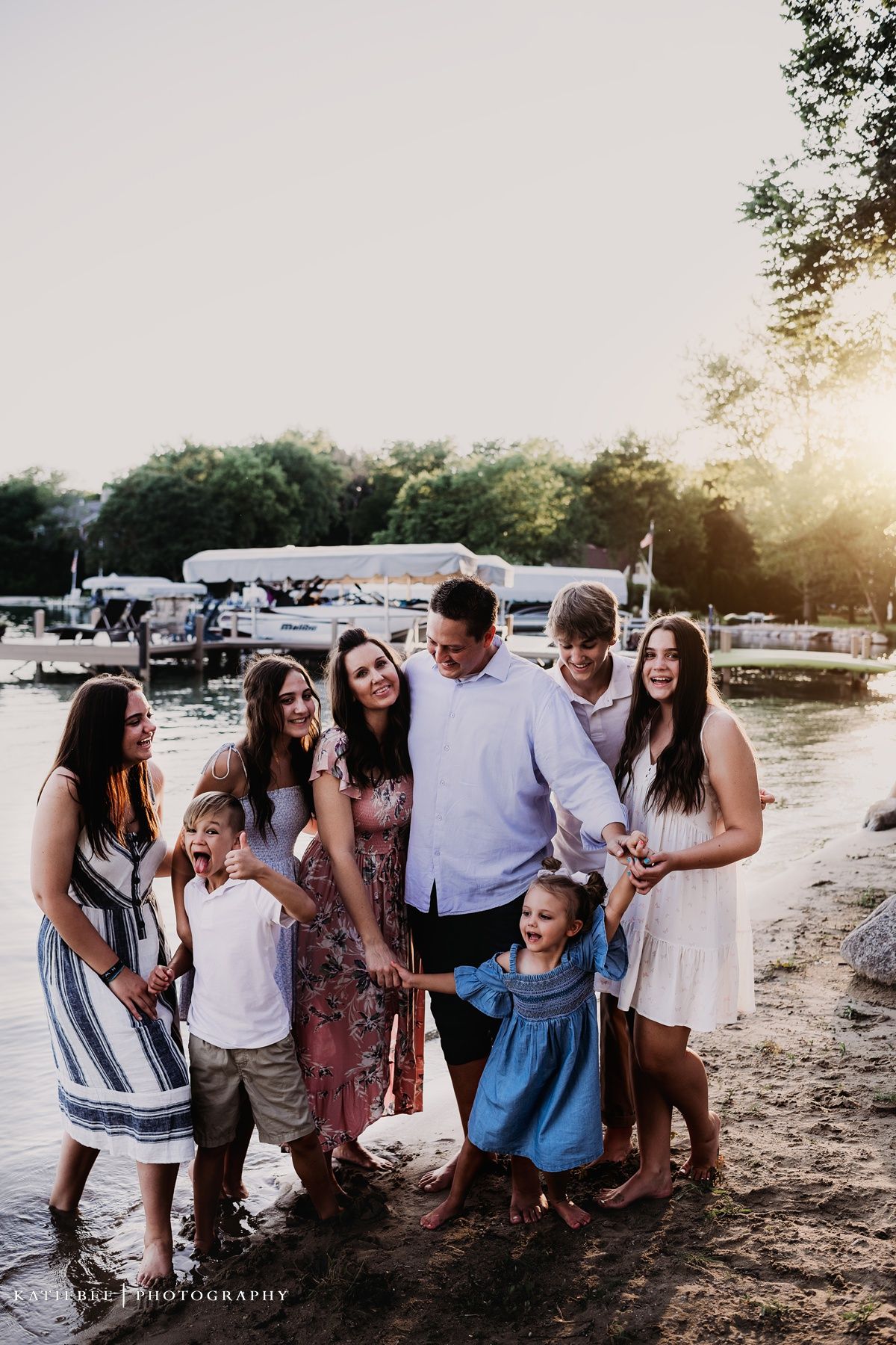 A family group poses together on a beach at sunset with boats in the background.