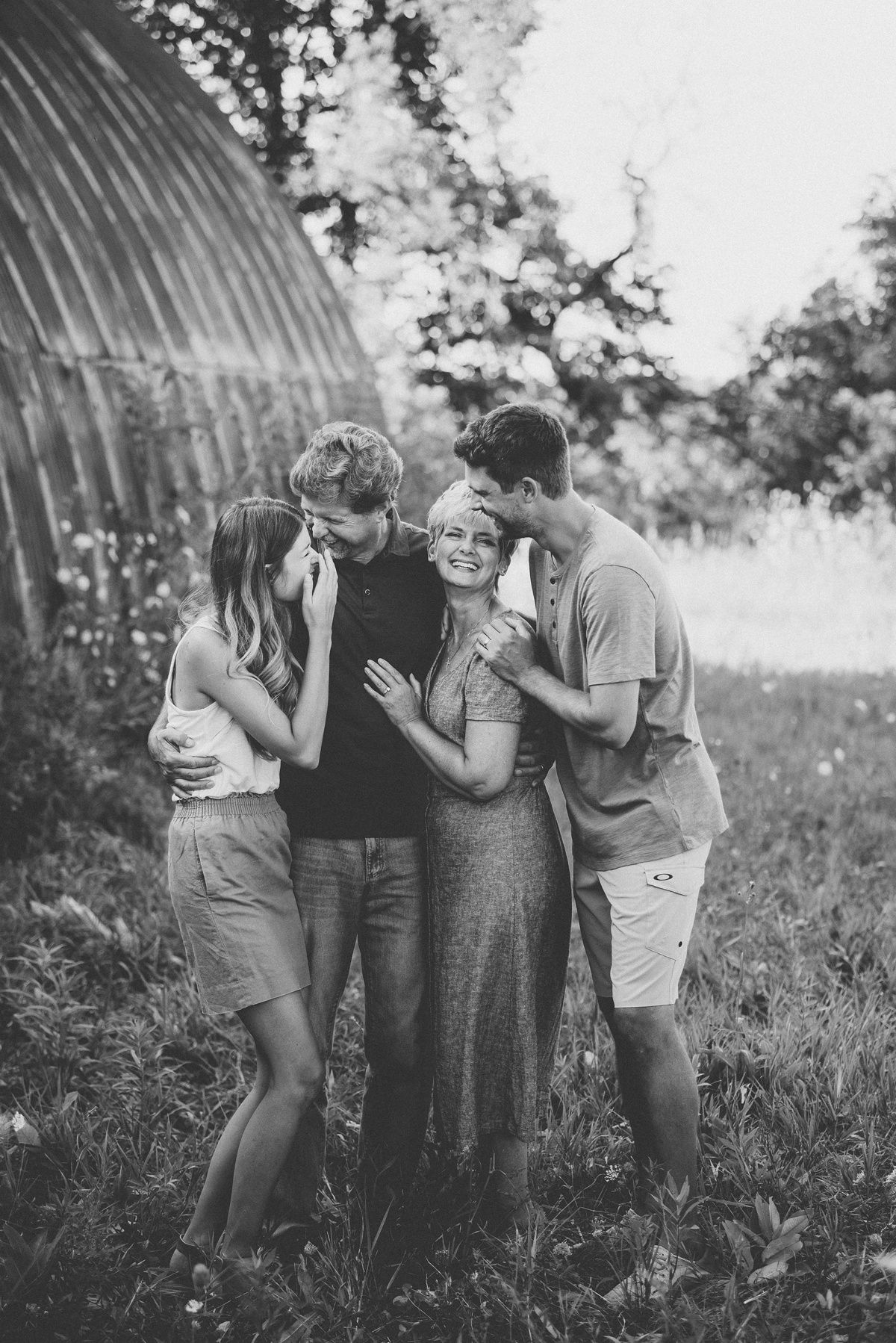 Intimate black and white family portrait against rustic barn exterior.