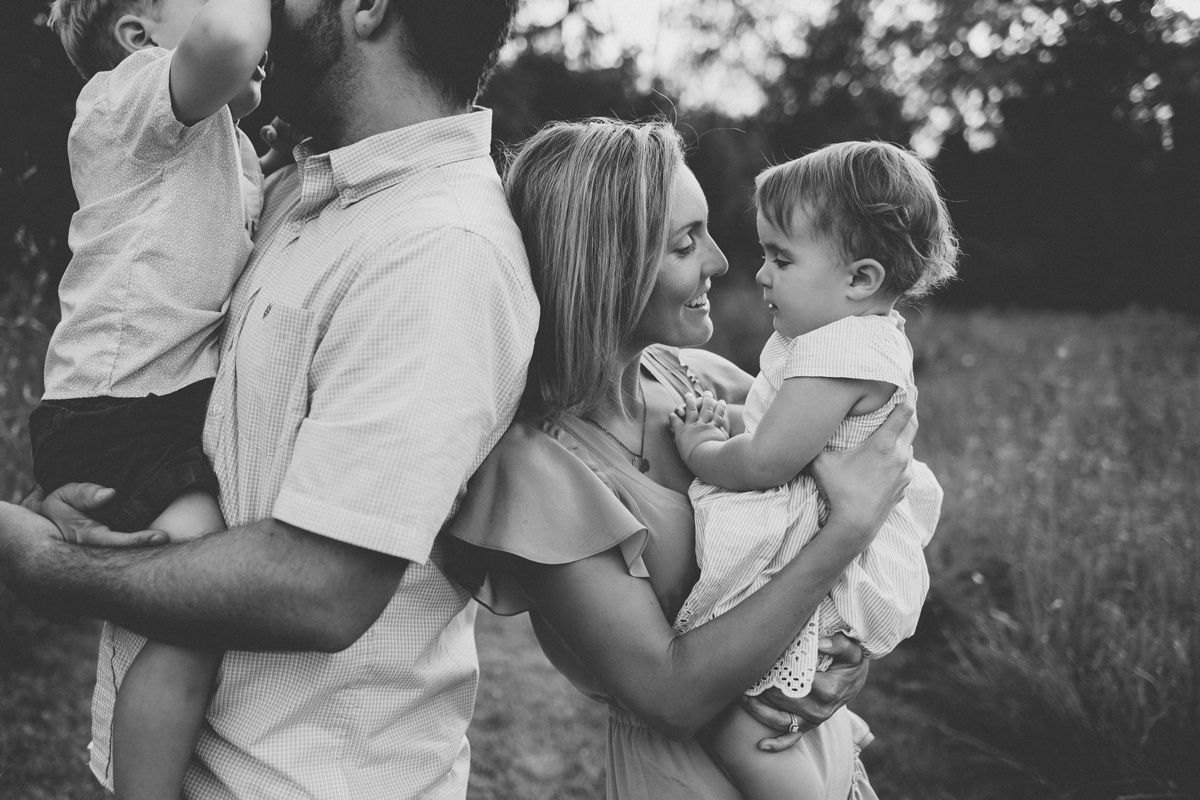 A tender black and white family moment captured outdoors in a natural setting.
