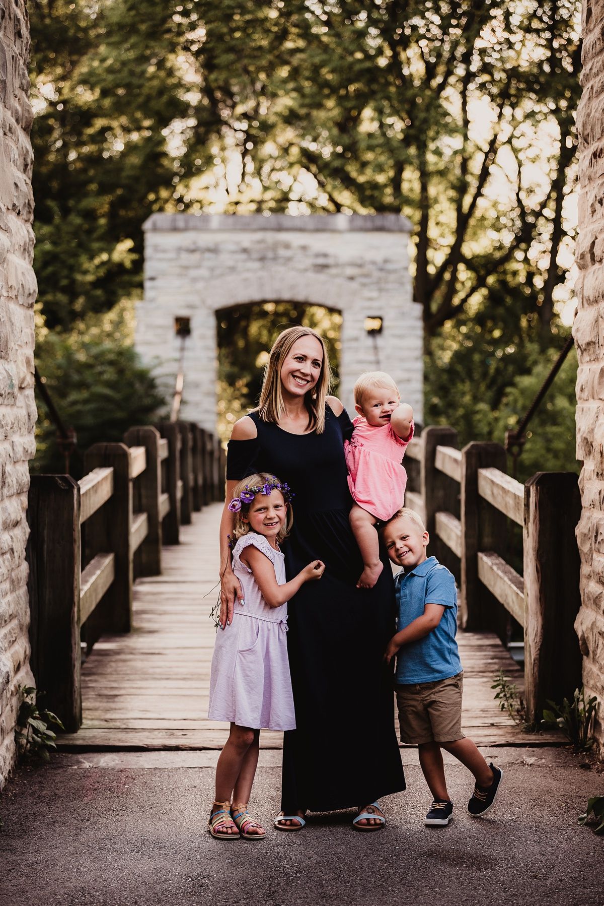 A family group portrait on a stone bridge walkway surrounded by trees.