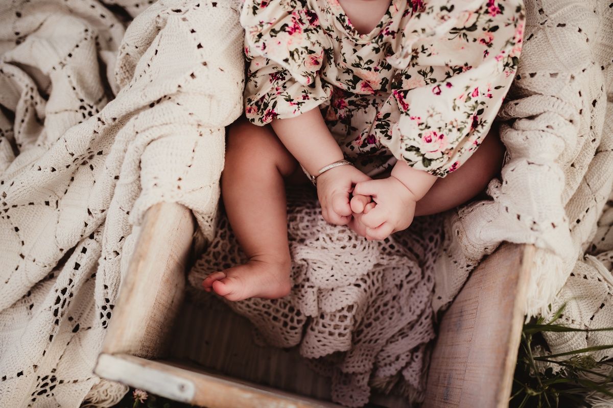 Close-up shot of tiny baby feet and floral dress details on textured cream blanket.