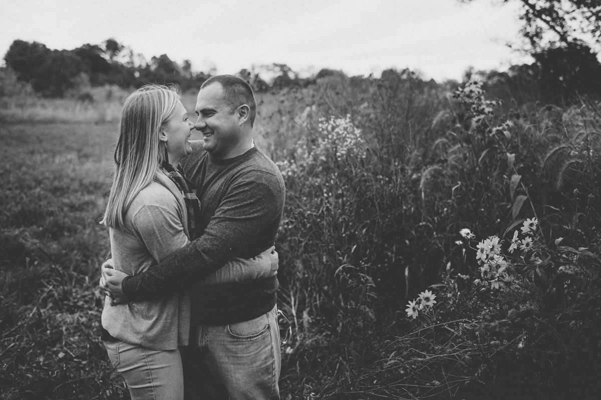 A black and white portrait of a couple embracing in a field with wildflowers.