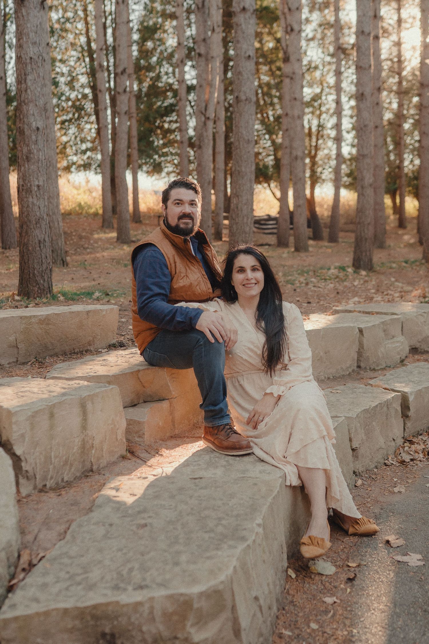 A couple sits together on stone steps surrounded by autumn trees in a park setting.