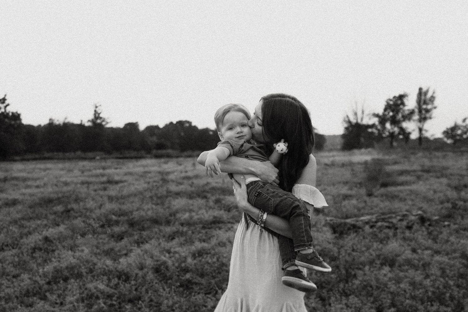 A tender moment between parent and child in a monochrome field setting at dusk.
