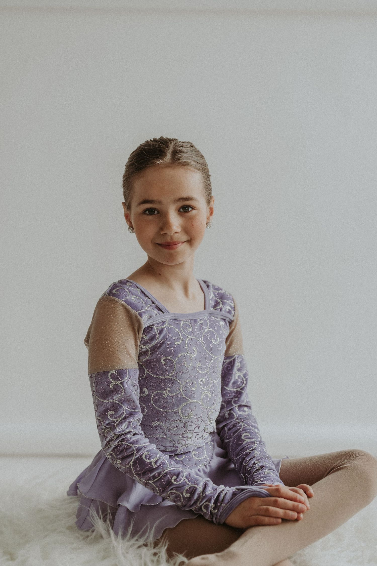Ballerina poses in a lavender dance costume with intricate pattern details on a white backdrop.