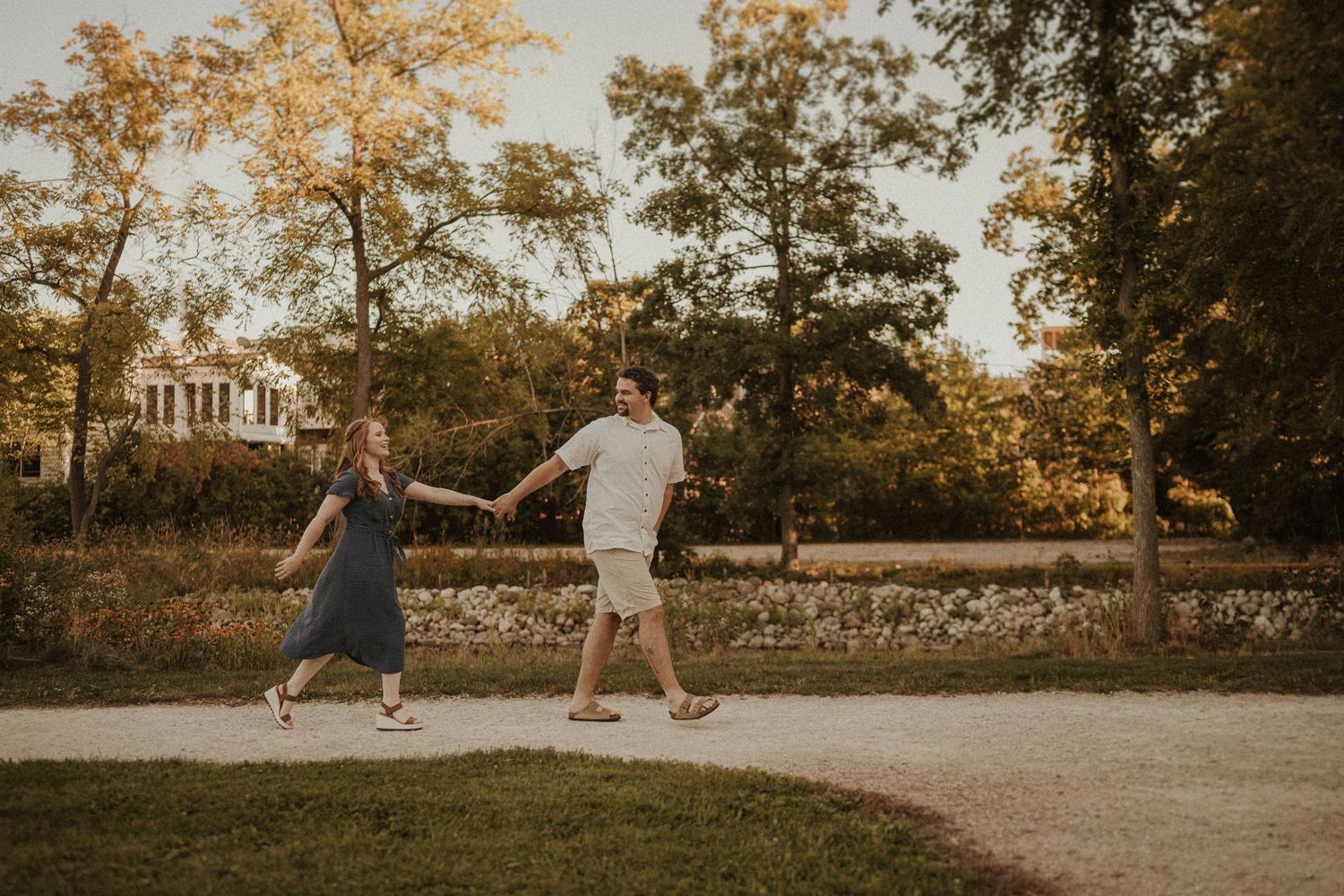 Playful couple holding hands while walking on a path during sunset.