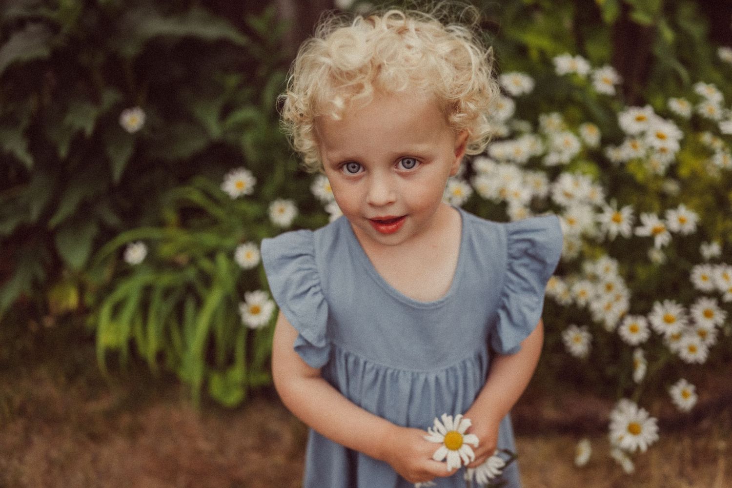 Close-up portrait in garden with blooming daisies and rustic background.