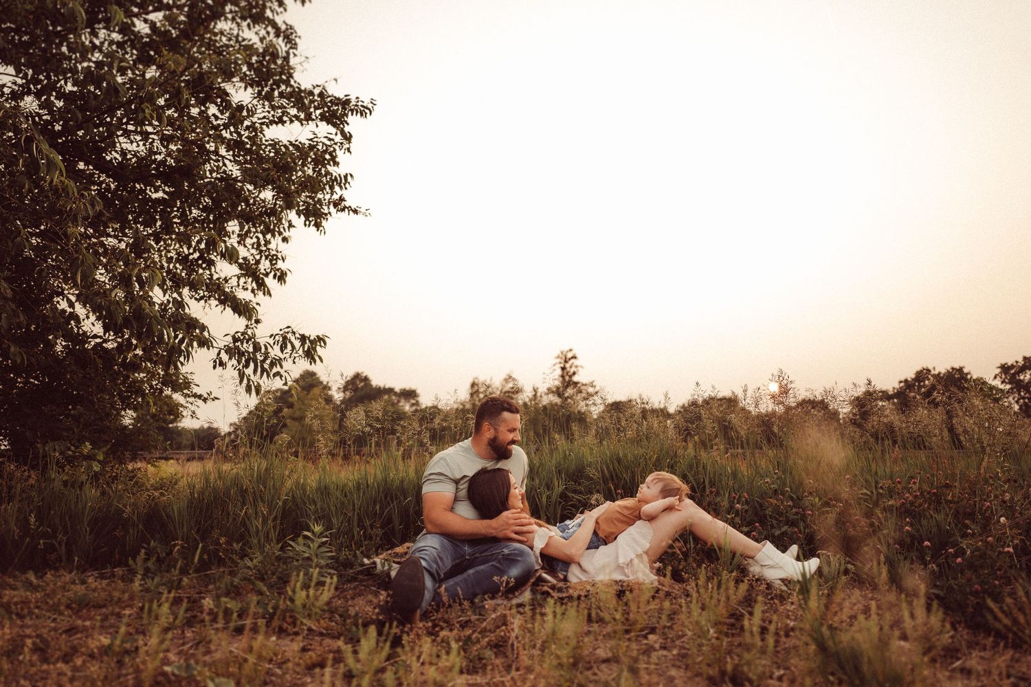 Family enjoying a peaceful moment together in a rustic field at sunset.