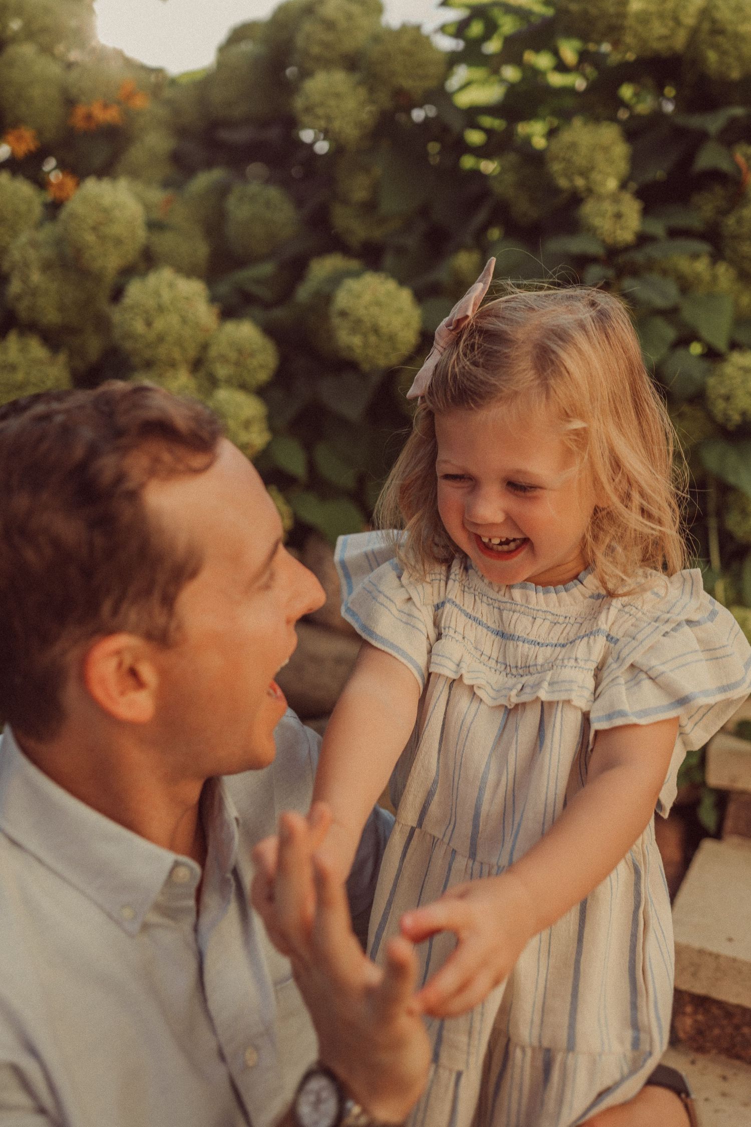 Joyful interaction between an adult and young child on garden steps with blooming hydrangeas in background.
