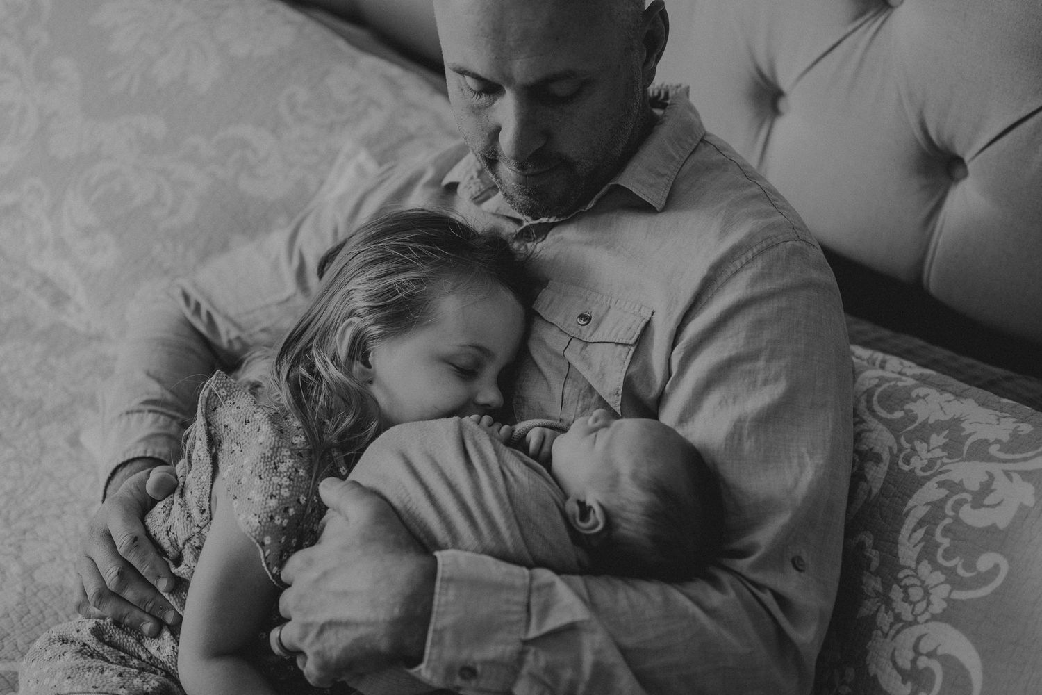 Black and white intimate family portrait on tufted headboard bed.