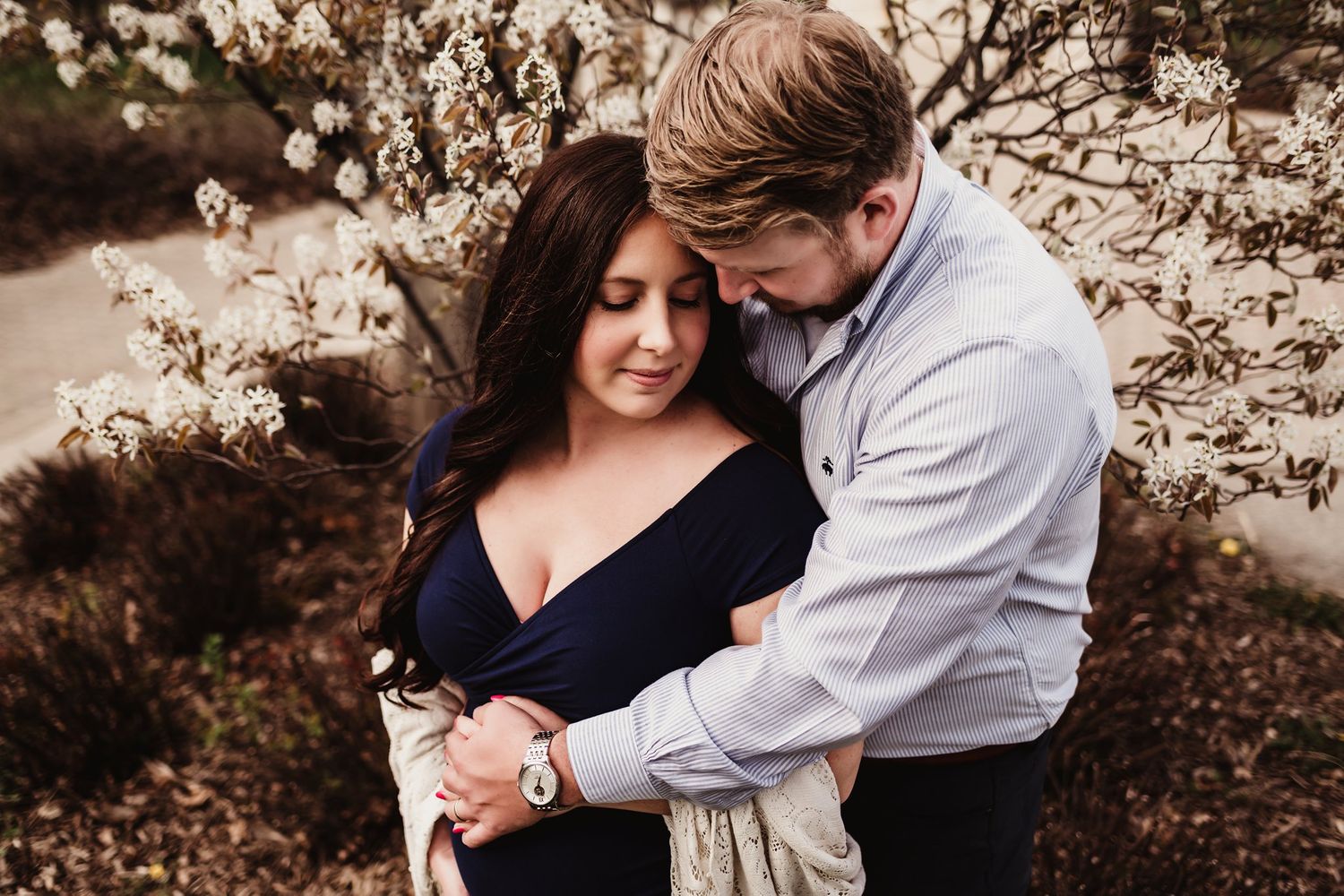 Romantic maternity photo of couple embracing among spring blossoms at sunset.