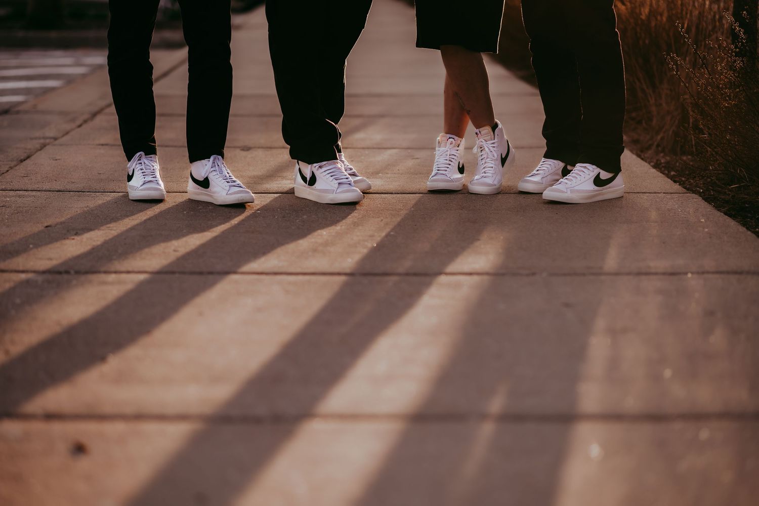 Row of people wearing white sneakers standing on wooden boardwalk at sunset.