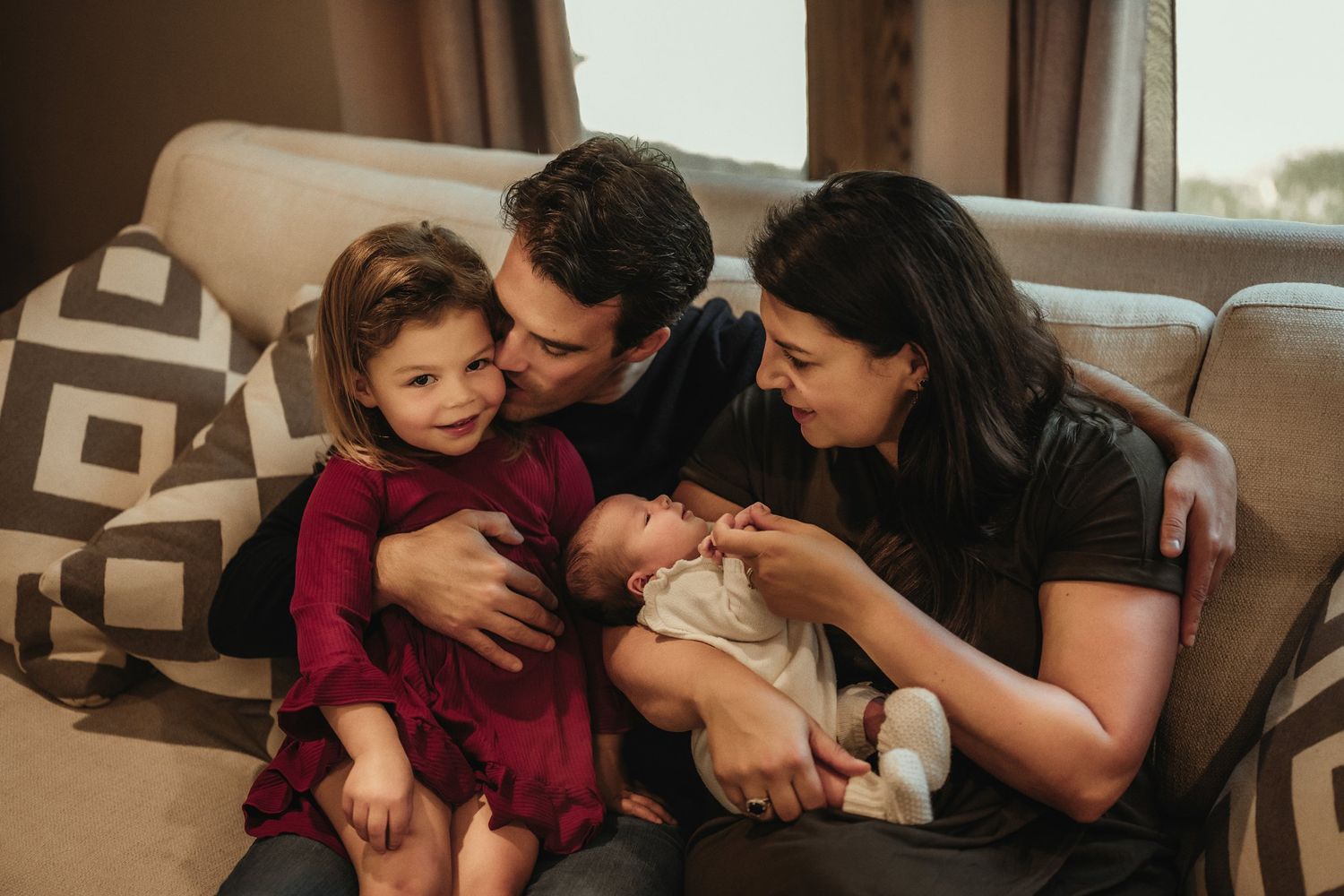 Family sharing an intimate moment together on a cozy brown couch with geometric patterned pillows.