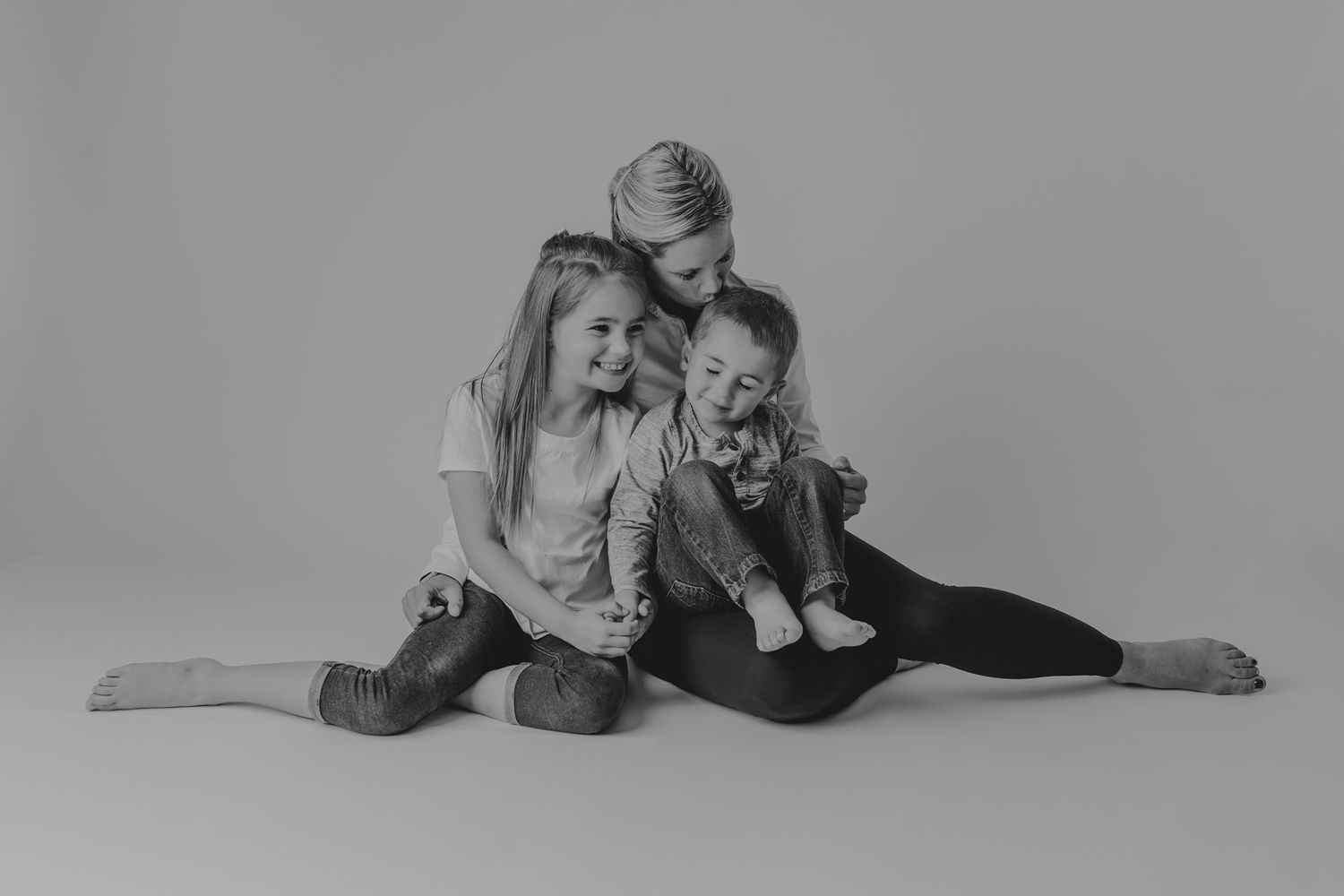 Black and white studio portrait showing intimate family moment during casual photo session.