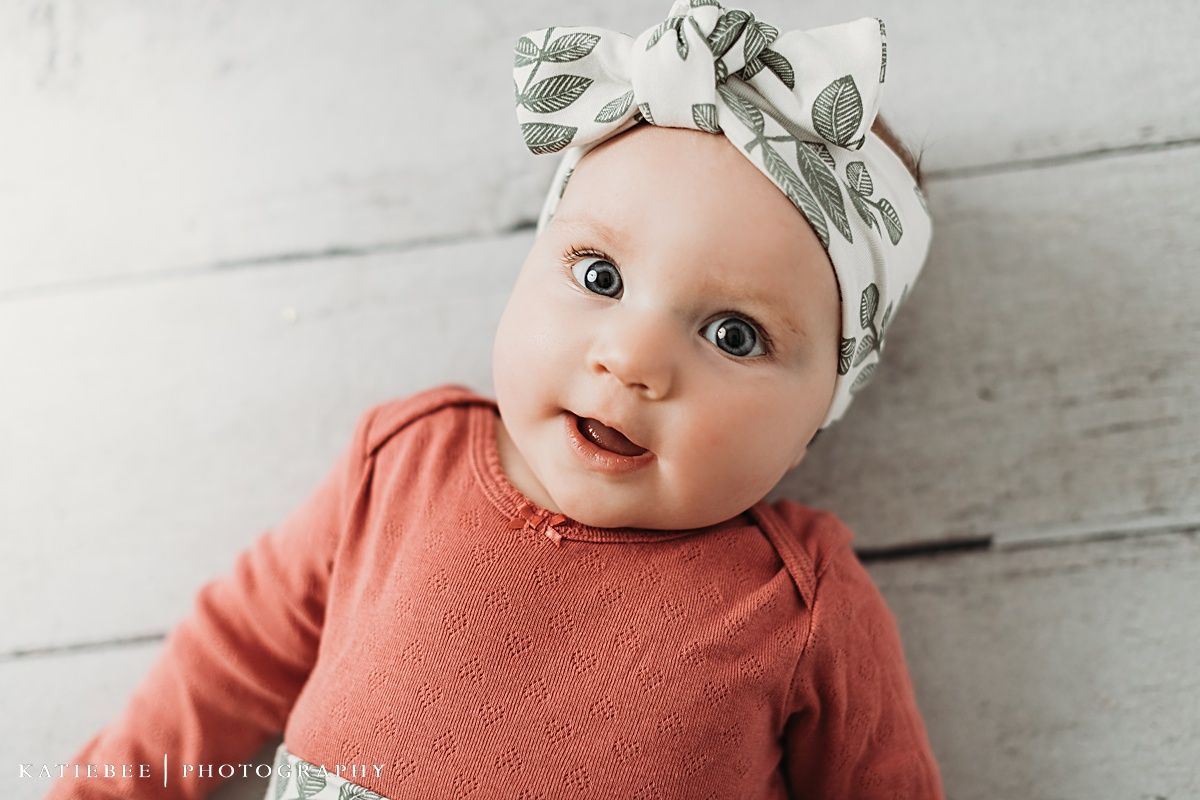 Baby in coral bodysuit and floral headband smiling during photo session.