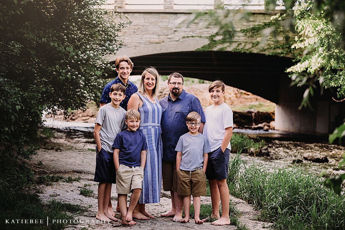 A family portrait taken under a stone bridge with everyone coordinated in blue and white outfits.