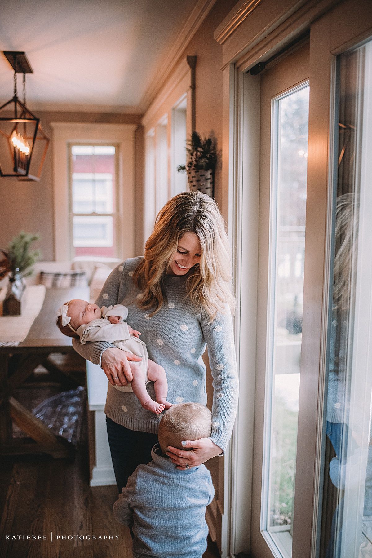 Lifestyle family photo near large windows with warm interior lighting and rustic decor.