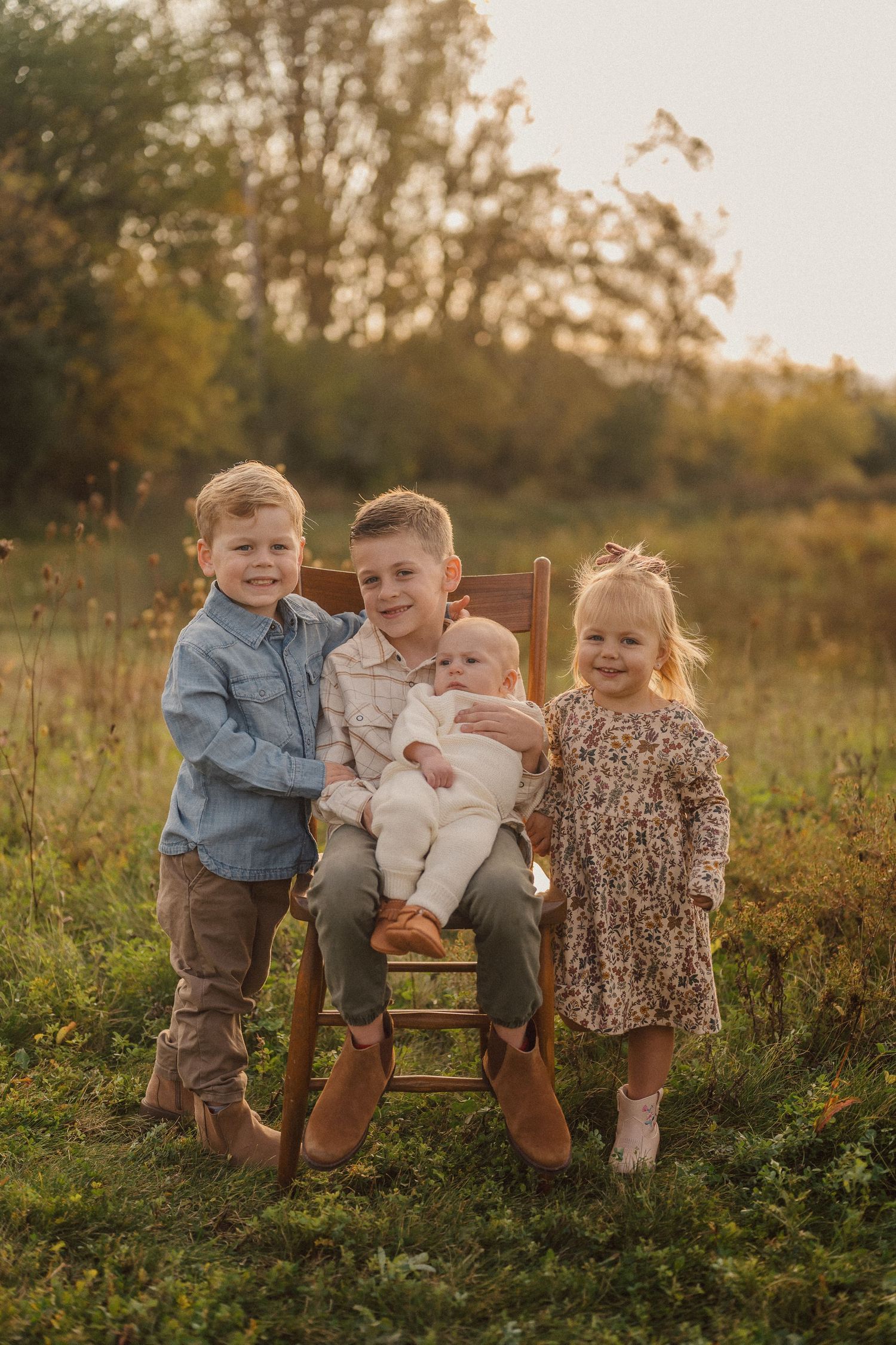 Children sitting together on a wooden chair in a golden autumn field at sunset.