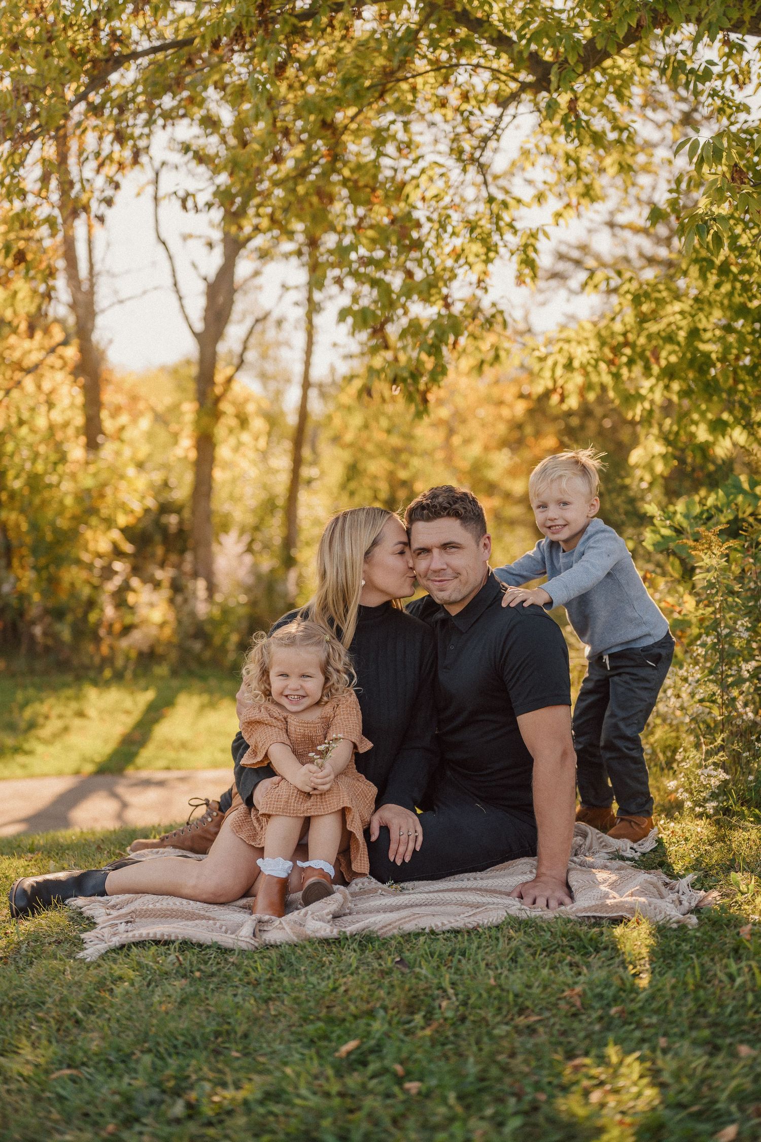 Family of four poses casually on a blanket outdoors during a warm autumn evening photoshoot.