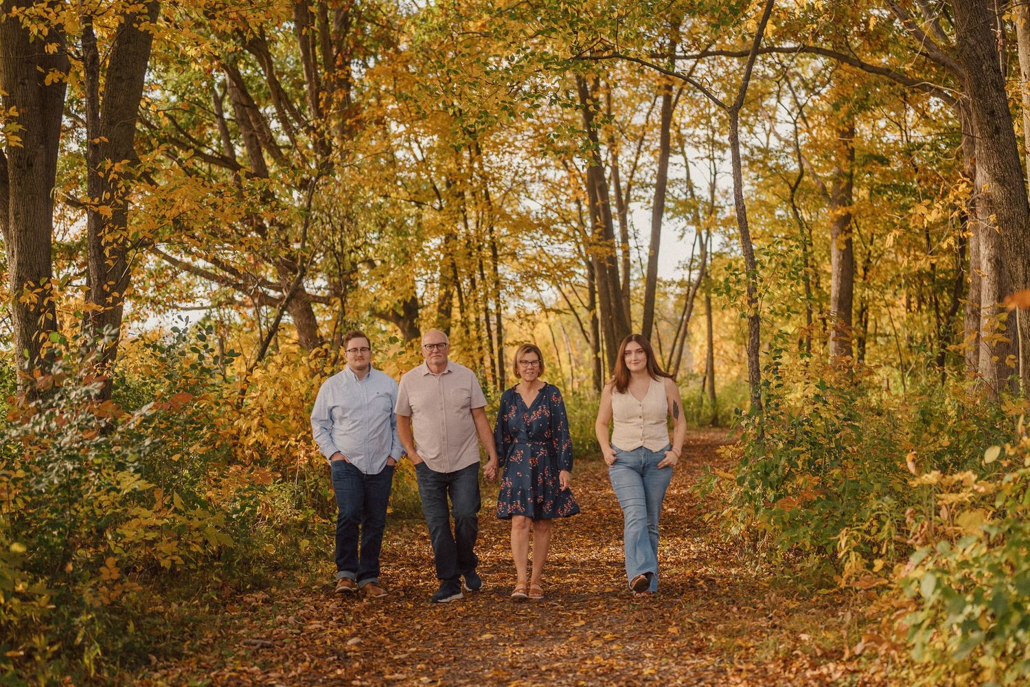 A group of people walking through a scenic autumn forest path with golden yellow foliage overhead.