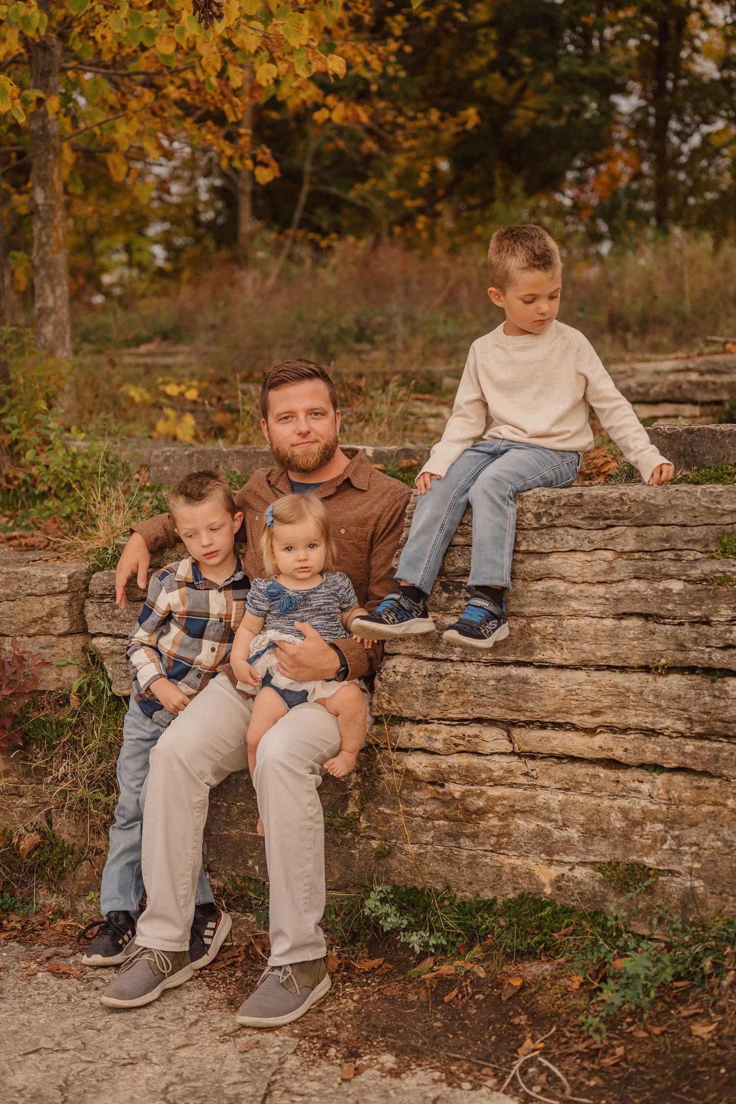 Family members sitting casually on stone ledge surrounded by fall colors.