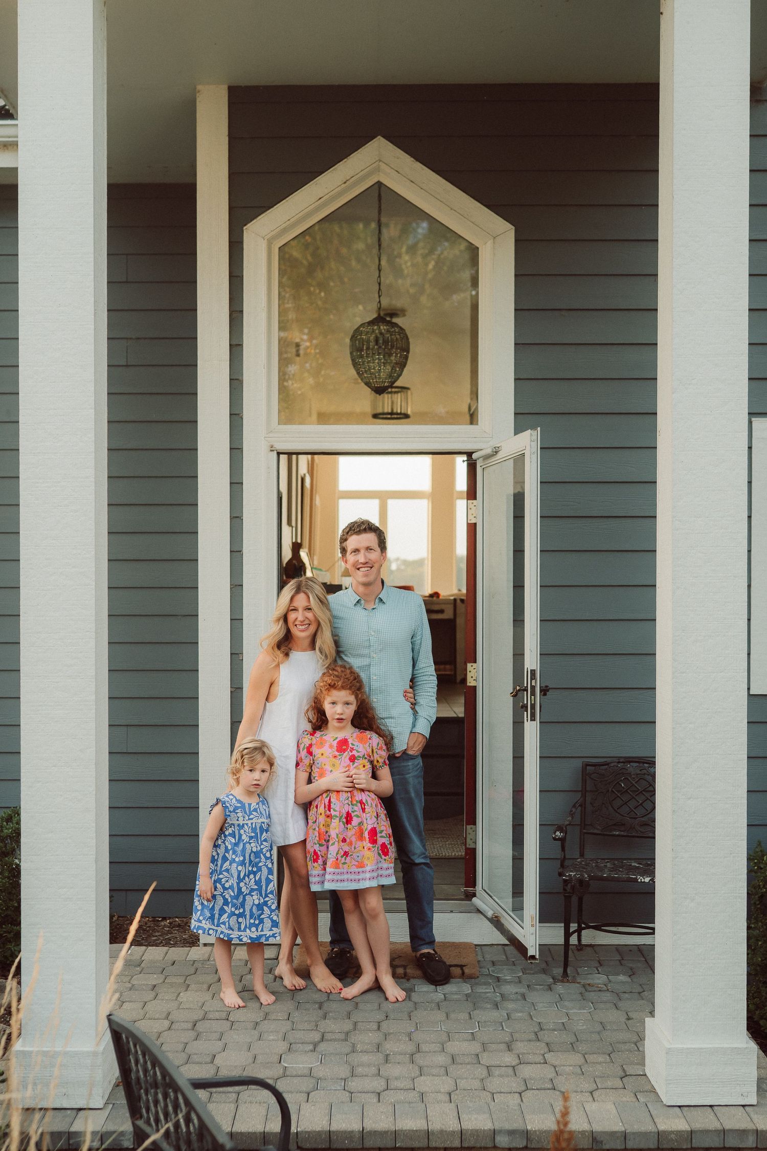 A family poses together in the doorway of their coastal-style home with white columns.